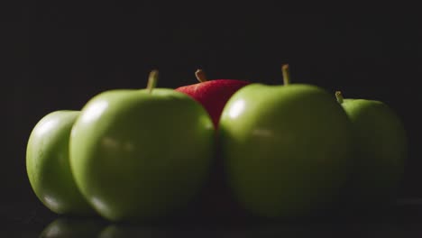 Studioaufnahme-Des-Roten-Apfels-Im-Kreis-Der-Grünen-Äpfel,-Die-Sich-Vor-Schwarzem-Hintergrund-Drehen