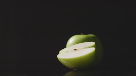 Studio-Shot-Of-Whole-And-Halved-Green-Apple-Revolving-Against-Black-Background