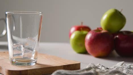 Apfelsaft-Wird-In-Glas-Mit-Eis-Und-Frischen-Äpfeln-Im-Hintergrund-Gegossen