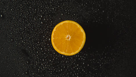 Overhead-Studio-Shot-Of-Orange-Half-With-Water-Droplets-Revolving-Against-Black-Background