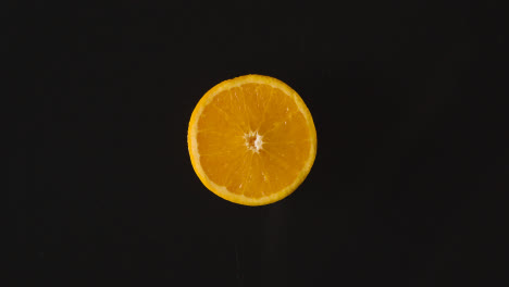 Foto-De-Estudio-Superior-De-La-Mitad-Naranja-Girando-Sobre-Fondo-Negro