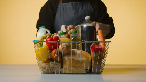 Studio-Shot-Of-Shop-Worker-Checking-Basic-Food-Items-In-Supermarket-Wire-Shopping-Basket-2