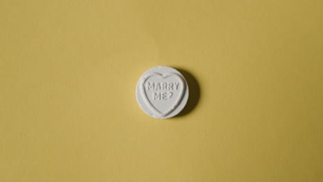Hand-Picking-Up-Heart-Candy-With-Marry-Me-Message-On-Yellow-Background