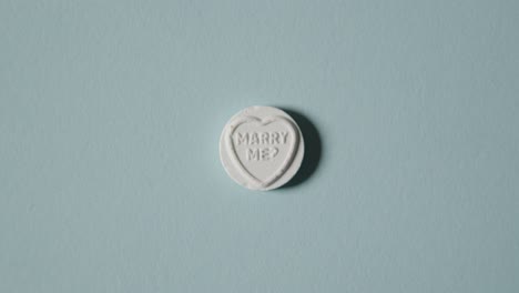 Hand-Picking-Up-Heart-Candy-With-Marry-Me-Message-On-Blue-Background