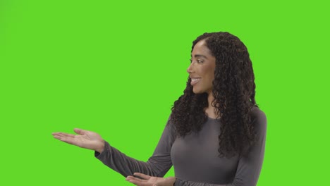 Portrait-Of-Woman-Presenting-Or-Demonstrating-Item-Against-Green-Screen-Smiling-At-Camera-1