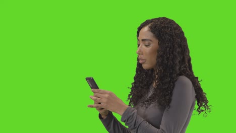Profile-Shot-Of-Woman-Text-Messaging-On-Mobile-Phone-Against-Green-Screen