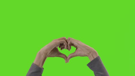 Studio-Close-Up-Shot-Of-Woman-Making-Heart-Shape-Symbol-For-Love-Against-Green-Screen