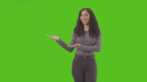 Portrait-Of-Woman-Presenting-Or-Demonstrating-Item-Against-Green-Screen-Smiling-At-Camera-2
