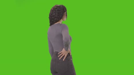 Rear-Three-Quarter-Length-Studio-Shot-Woman-Standing-Against-Green-Screen-With-Hand-On-Hips