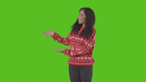Studio-Portrait-Of-Woman-Wearing-Christmas-Jumper-Showing-Item-Or-Object-Against-Green-Screen-Smiling-At-Camera