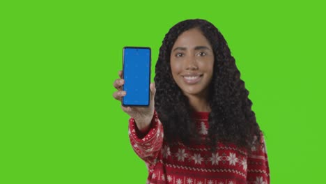 Studio-Portrait-Of-Woman-Wearing-Christmas-Jumper-Holding-Up-Mobile-Phone-Against-Green-Screen-2
