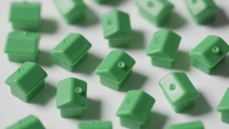 Home-Buying-Concept-With-Hand-Clearing-Away-Group-Of-Green-Plastic-Models-Of-Houses-Revolving-On-White-Background-