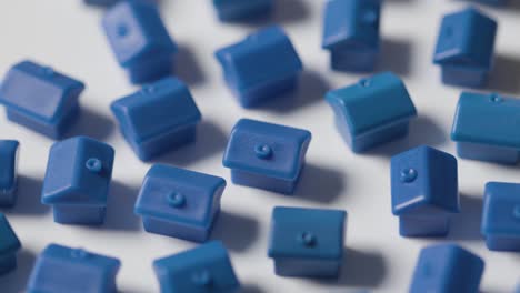 Home-Buying-Concept-With-Hand-Clearing-Away-Group-Of-Blue-Plastic-Models-Of-Houses-Revolving-On-White-Background-