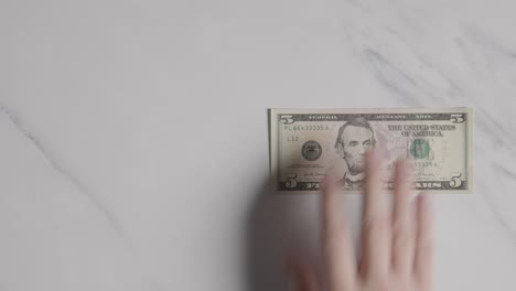 Overhead-Currency-Shot-Of-Hand-Grabbing-US-5-Dollar-Bill-On-Marble-Surface