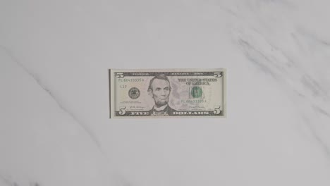 Overhead-Currency-Shot-Of-Hand-Grabbing-US-5-Dollar-Bill-On-Marble-Surface-1