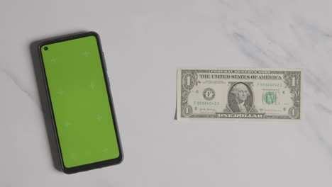 Overhead-Currency-Shot-Of-US-1-Dollar-Bill-Next-To-Green-Screen-Mobile-Phone