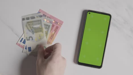 Overhead-Currency-Shot-Person-Counting-Euro-Notes-And-Coins-Next-To-Green-Screen-Mobile-Phone-1