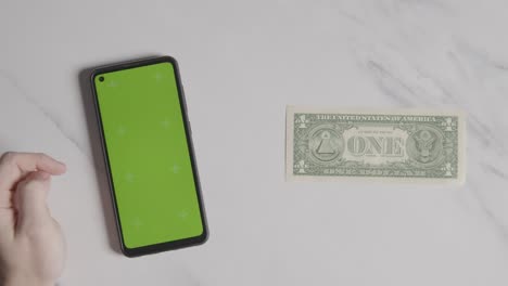 Overhead-Currency-Shot-Of-US-1-Dollar-Bill-Next-To-Person-Using-Green-Screen-Mobile-Phone-1