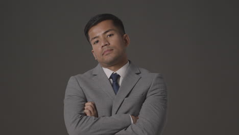 Studio-Portrait-Of-Serious-Businessman-In-Suit-Against-Grey-Background-Looking-At-Camera