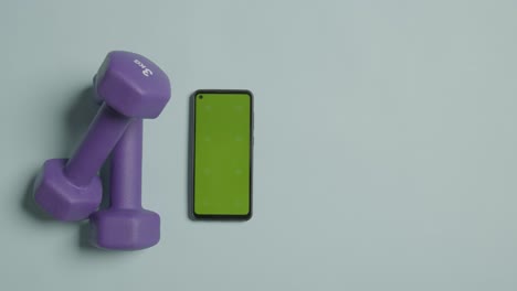 Overhead-Fitness-Studio-Shot-Of-Male-Hand-Picking-Up-Exercise-Dumbbell-Weights-Next-To-Green-Screen-Mobile-Phone-4