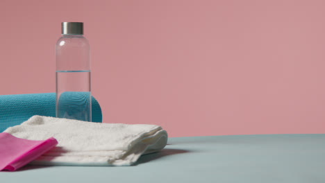 Fitness-Studio-Shot-Of-Water-Bottle-With-Exercise-Mat-And-Towel-Against-Pink-Background-1
