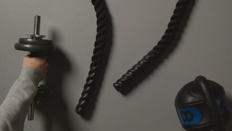 Overhead-Studio-Fitness-Shot-Of-Battle-Rope-On-Grey-Background-With-Hand-Picking-Up-Gym-Weight-1