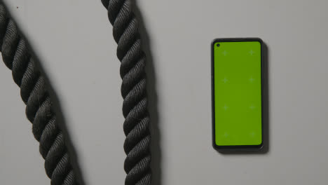 Overhead-Studio-Fitness-Shot-Of-Hands-Picking-Up-Gym-Battle-Ropes-With-Green-Screen-Mobile-Phone-On-Grey-Background-1