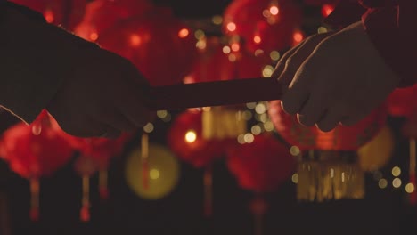 Hands-Exchanging-Card-Celebrating-Chinese-New-Year-With-Chinese-Lanterns-Hung-In-Background-