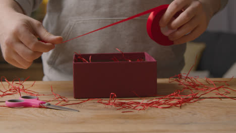 Close-Up-Of-Man-At-Home-Cutting-Ribbon-To-Gift-Wrapping-Romantic-Valentines-Present-In-Box