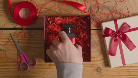 Overhead-Shot-Of-Man-Gift-Wrapping-Romantic-Valentines-Present-Of-Perfume-In-Box-On-Table