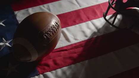 Studioaufnahme-Einer-Person,-Die-American-Football-Mit-Helm-Auf-Der-Stars-And-Stripes-Flagge-Aufhebt