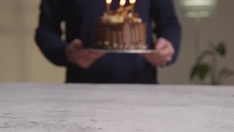 Close-Up-Shot-Of-Person-At-Home-Carrying-Decorated-Chocolate-Birthday-Celebration-Cake-With-Lit-Candles