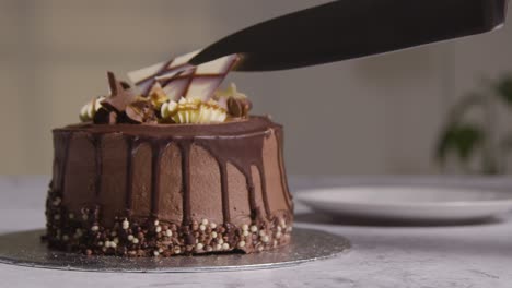 Close-Up-Shot-Of-Person-At-Home-Cutting-Slice-From-Chocolate-Celebration-Cake-On-Table