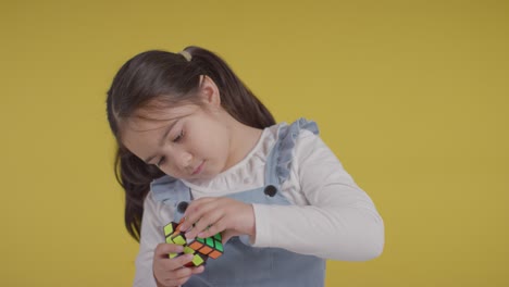 Studioporträt-Eines-Jungen-Mädchens-Auf-Dem-ASD-Spektrum,-Das-Einen-Puzzlewürfel-Vor-Gelbem-Hintergrund-Löst-1