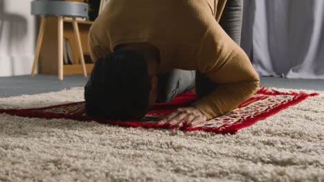 Hombre-Musulmán-En-Casa-Arrodillado-En-La-Alfombra-De-Oración-Y-Rezando