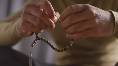 Nahaufnahme-Eines-Betenden-Muslimischen-Mannes-Mit-Gebetsperlen,-Der-Zu-Hause-Auf-Dem-Boden-Sitzt-1
