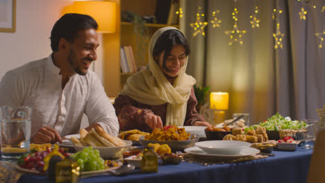 Muslimische-Familie-Sitzt-Zu-Hause-Am-Tisch-Mit-Einer-Frau,-Die-Biryani-Beim-Essen-Serviert,-Um-Eid-1-Zu-Feiern
