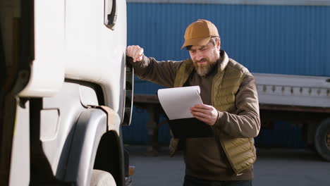 Worker-Wearing-Vest-And-Cap-Reading-Documents-In-A-Logistics-Park-While-Is-Leaning-On-A-Truck