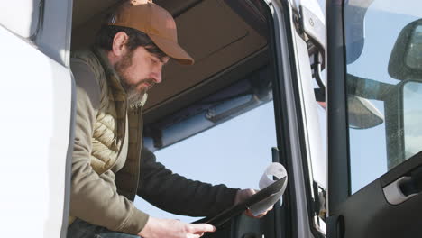 Worker-Wearing-Vest-And-Cap-Organizing-A-Truck-Fleet-In-A-Logistics-Park-While-Reading-Documents-In-A-Truck-1
