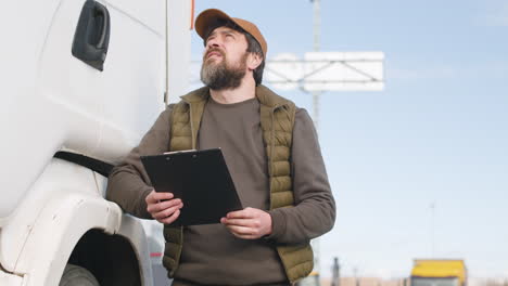 Worker-Wearing-Vest-And-Cap-Reading-Documents-In-A-Logistics-Park-While-Is-Leaning-On-A-Truck-1