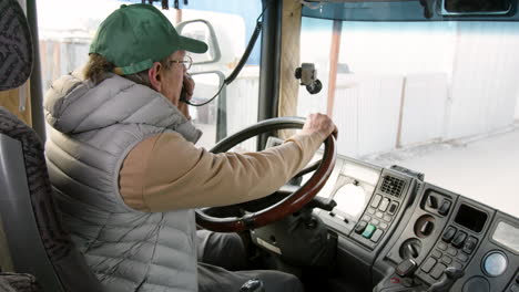Side-View-Of-Older-Worker-Sitting-In-A-Truck-In-A-Logistics-Park-While-Talking-On-The-Radio