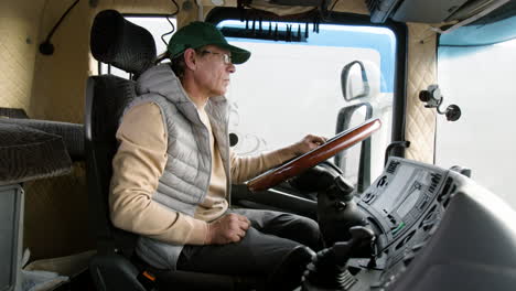 Side-View-Of-Older-Worker-Wearing-Cap-And-Vest-Driving-A-Truck-In-A-Logistics-Park-3