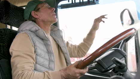 Bottom-View-Of-Older-Worker-Wearing-Cap-And-Vest-Driving-A-Truck-In-A-Logistics-Park