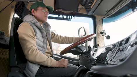 Side-View-Of-Older-Worker-Wearing-Cap-And-Vest-Driving-A-Truck-In-A-Logistics-Park-6