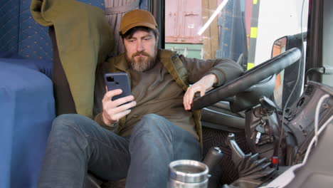 Worker-Wearing-Cap-And-Vest-Tumbado-Lying-On-Truck-Seat-While-Using-Smartphone