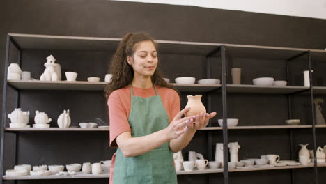 Smiling-Female-Clerk-Holding-A-Clay-Jug-And-Taking-Photo-In-The-Pottery-Shop