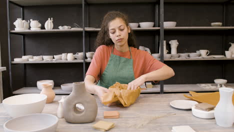 Junge-Frau,-Die-Handwerkliche-Keramik-Mit-Papier-Einwickelt,-Während-Sie-Am-Tisch-In-Der-Töpferei-Sitzt