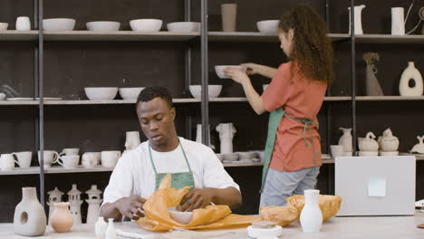 Young-Man-Packaging-Handicraft-Ceramics-With-Paper-In-The-Pottery-Shop-While-His-Female-Colleague-Helping-Him