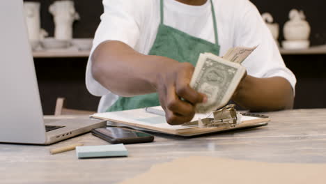 Male-Small-Business-Owner-Counting-Money-And-Writing-On-Clipboard-In-The-Pottery-Shop-1