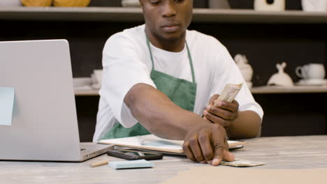 Male-Small-Business-Owner-Counting-Money-And-Using-Phone-Calculator-In-The-Pottery-Shop